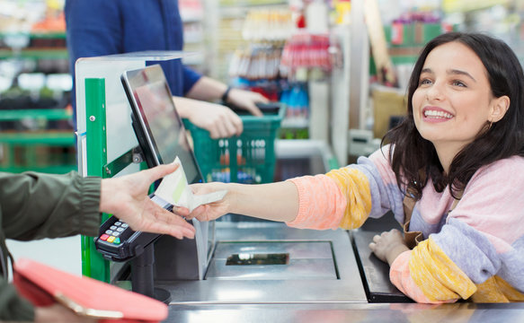 Smiling female cashier receipt to customer at supermarket checkout