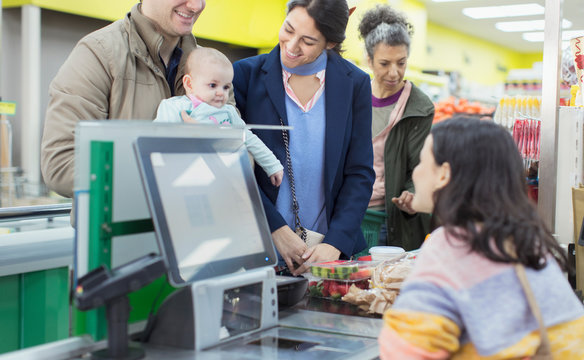 Friendly cashier helping couple with baby at supermarket checkout
