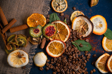 dark decorated table with coffee beans, dry oranges,dry lemons,dry Sabras fruit,dry kiwi,cinnamon sticks . View from above.place for the text.