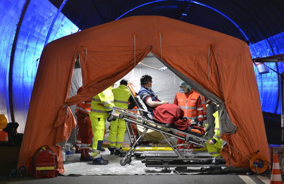 Alert Covid-19. Man on stretcher is visited inside a temporary hospital field tent for the first AID for patient with Corona Virus. Zone for inspection in public place for people infected people. 