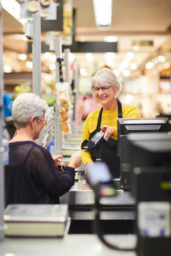 Senior female cashier helping customer at supermarket checkout