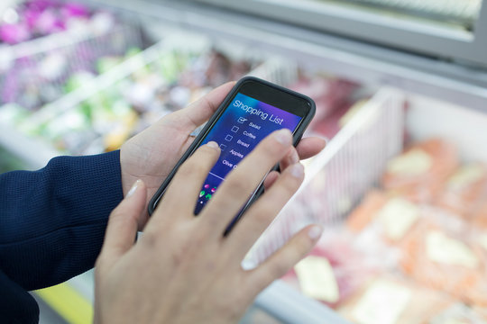Close up woman using smart phone shopping list app in supermarket