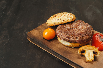 Grilled burger cutlet with a bun on wooden board, top view