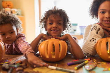 Portrait happy brother and sisters carving pumpkins at table