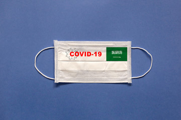 Flag of Saudi Arabia and inscription COVID-19 on a medical mask on a blue background. Healthcare and medical concept. Pandemic virus COVID-19