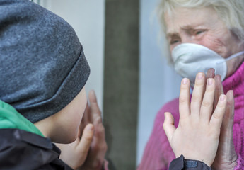 A crying grandmother mature woman in a respiratory mask communicates with grandchild through a...