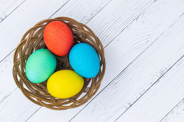 Four Easter colored plain eggs. A set of homemade eggs for Happy Easter holiday on a white wooden background. Boiled colorful cooked eggs in a wicker basket top view