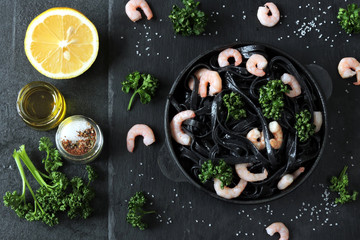 Black pasta with shrimp and parsley on a graphite black surface. Minimalistic black food. Black food concept.