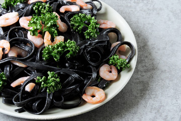 Black pasta with shrimp and parsley on a graphite black surface. Minimalistic black food. Black food concept.