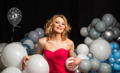 Fototapeta premium Lady in red. Beautiful smiling woman with balloon. Celebrating new year, Christmas, x-mas, birthday, b-day. Portrait of pretty charming girlfriend having air balloons.