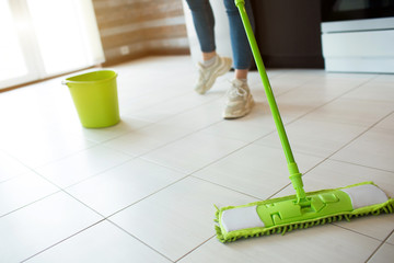Young woman on kitchen during quarantine. Cleaning floor with green mop. Low cut view. Making floor more clean. Green bucket with water behind. © Vlad