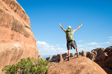 Unrecognizable hiker standing outdoors with arms raised on the top of a red rock mountain landscape