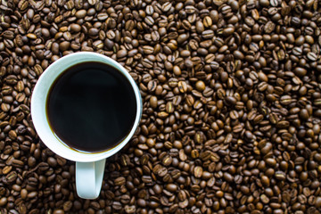 White Cup with black espresso on scattered coffee beans close up top view with copy space