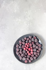 Frozen berries (blackberries and raspberries), covered with hoarfrost on a black ceramic plate. Home harvest. 