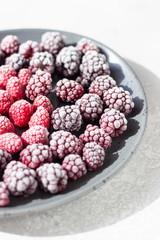 Frozen berries (blackberries and raspberries), covered with hoarfrost on a black ceramic plate. Home harvest. 