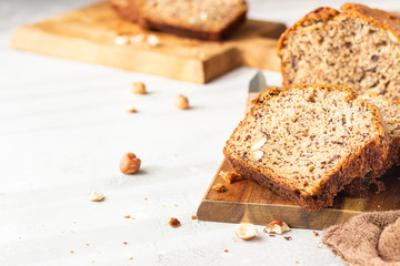 Homemade banana bread or cake with hazelnut on wooden cutting board, light stone background. Trendy...