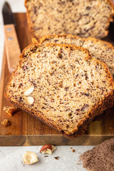 Homemade banana bread or cake with hazelnut on wooden cutting board, light stone background. Trendy soft shadows, atmospheric lighting, selective focus. Flat lay composition.
