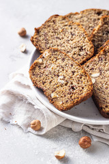 Sliced hazelnuts and banana loaf cake on a ceramic plate. Selective focus, top view.