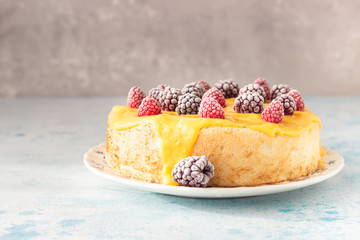 Angel food cake with lemon curd and frozen berries (raspberry and blackberry) on a plate, blue concrete background. Homemade chiffon cake.