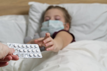 A young girl lying on the bed is given pills and a glass of water. masked girl for protection against viral diseases. concept of quarantine and treatment for viral diseases, colds and coronavirus