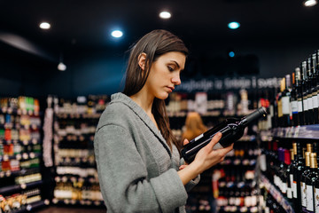 Woman shopping for expensive wine in supermarket alcohol store.Choosing and buying good cheap...