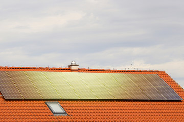 Photovoltaic or solar panels on roof of the house at sunset. Red roof with ecological solar system...