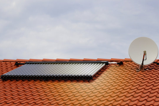 Photovoltaic or solar panels for water system on roof. House at sunset. Red roof with ecological solar system during the summer day. Clouds in the background.