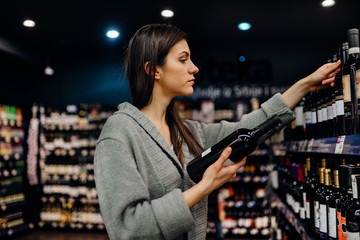 Woman shopping for expensive wine in supermarket alcohol store.Choosing and buying good cheap...