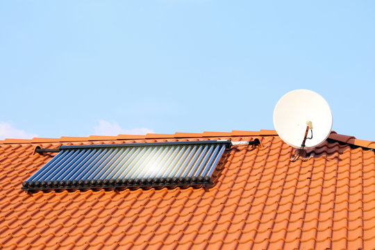 Photovoltaic or solar panels for water system on roof. House at sunset. Red roof with ecological solar system during the summer day. Clouds in the background.