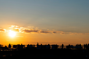 Fototapeta premium Silhouettes of young people sitting on the St. Petersburg roof against the background of the orange sunset