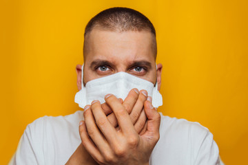 Closeup portrait of a young guy wearing a respirator on a yellow background. Coughing in hands. Respiratory tract disease. Symptoms of coronavirus. Flu outbreak.