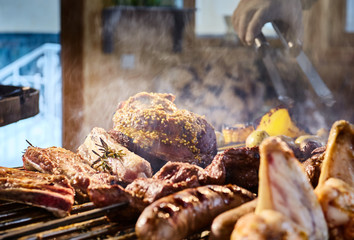The meat is pickled on a lattice grill, ribs spread, a stake, Sausages, edges, chicken, naked flame, black pepper, a smoke, firewood, hands of the chef display meat, Hands in gloves, close up