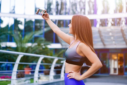 Young gorgeous sportswoman standing in public park and taking a selfie after exercising