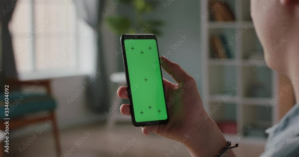 Wall mural man using a mobile phone with chroma key green screen, watching a video or having an online conferen