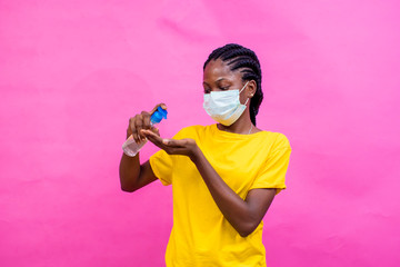 a young pretty african girl wearing a face   mask and using her hand sanitizer.