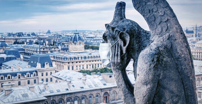 COVID-19 coronavirus in France, medical mask on gargoyle of Notre Dame in Paris. Tourist landmarks closed due to corona virus outbreak.