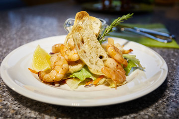 Grilled shrimp is on white plate with toasts, lemon and sauce, Thyme branch, leaf of salad