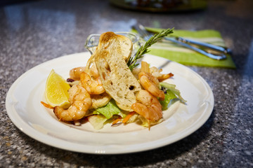 Grilled shrimp is on white plate with toasts, lemon and sauce, Thyme branch, leaf of salad
