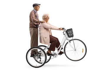 Fototapeta na wymiar Senior woman riding a tricycle and a senior man behind her