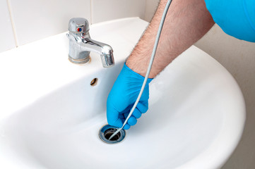 Plumbing issues, occupation in sanitation and handyman contractor concept with plumber repairing drain with plumbers snake (steel spiral that twists through pipes to collect dirt) in residential sink - 334607671