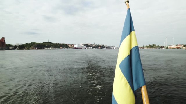 Sweden flag waving in the wind on ship aft stern feed flagpole sailing in Stockholm city center harbour