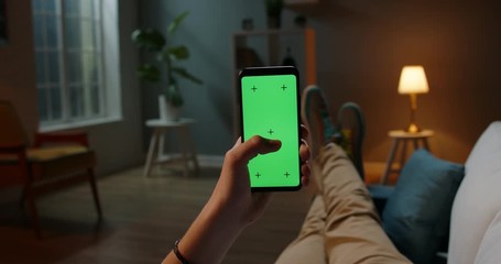 Man lying on couch using smartphone with chroma key green screen at night, scrdoing various gestures like swiping and scrolling - internet, communications concept close up 4k template - Powered by Adobe