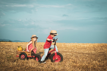 Funny little couple with vintage bike. Childhood memories. Happy children farmers cycle on spring field. Active children concept. Nature and children lifestyle. Children farmer concept. Eco living.