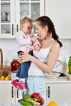 Young mother feeds child in the kitchen.