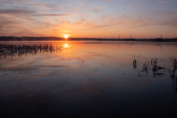 Gorgeous sunrise over the lake with reflection of the sun on the lake and spring