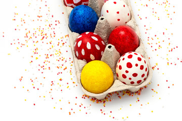 Color Easter eggs in a paper box on a white background with colored sugar sprinkles