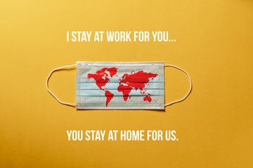 Surgical mask with a red map of the world, with message "STAY AT HOME " Concept of global spread  Covid-19. Coronavirus pandemic. yellow  background, nobody