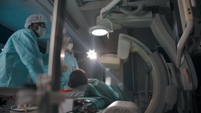 Dark-skinned and caucasian surgeons discussing about operation in operating room. Slow motion wide camera movement under surgical table.