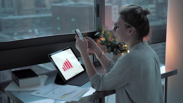 Millennial female messaging on cellphone device during statistic accounting on tocu pad, Caucasian freelancer communicating via smartphone gadget for consulting about financial graphs
