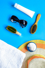 Summer cosmetic with protection cream and hat blue background top view